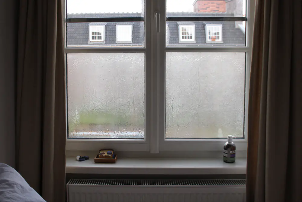 Condens op de binnenkant van een raam in een koude slaapkamer, druppels lopen over het glas