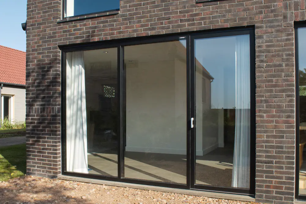 Slanke zwarte aluminium kozijnen met grote ruiten in een moderne gevel van lichte baksteen