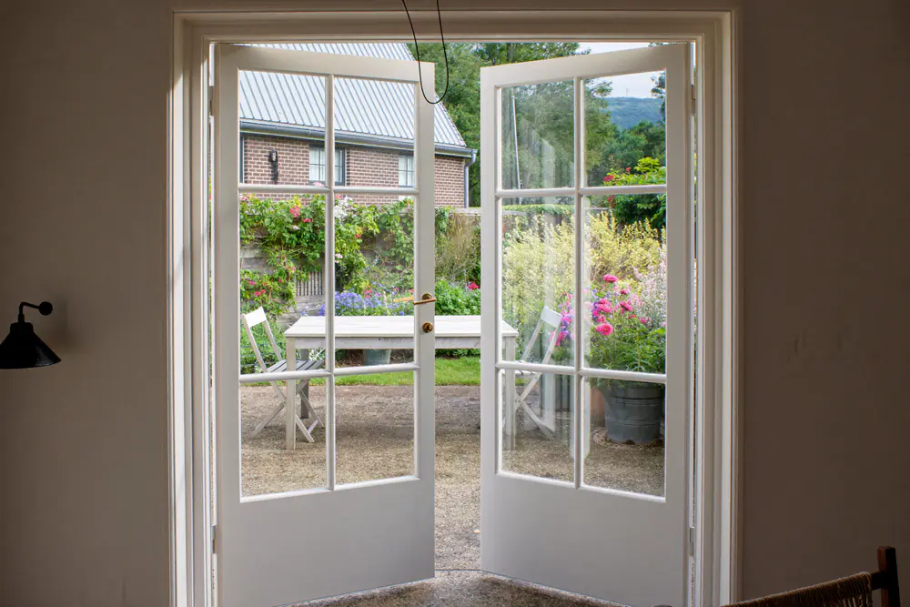 Witte openslaande tuindeuren naar een terras met een tafel en twee stoelen