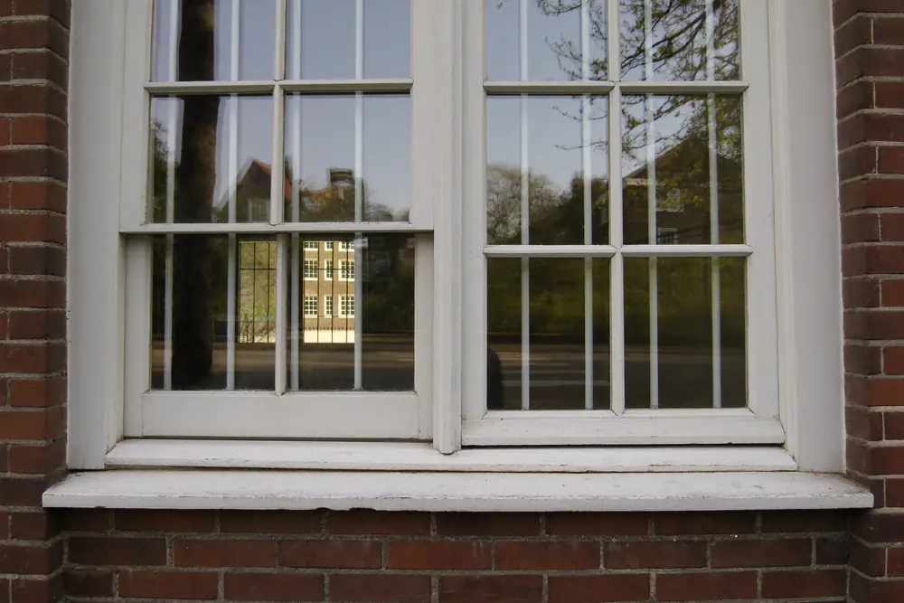 Oud wit houten raam met roedes in een bakstenen muur, waar een voorzetraam voor kan