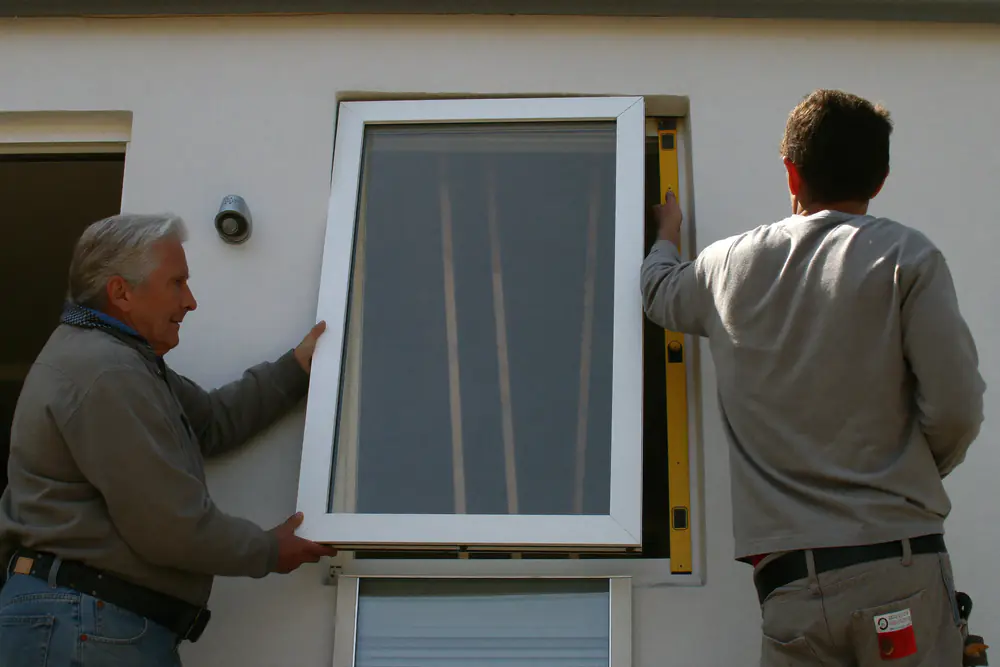 Twee monteurs tillen een nieuw kunststof kozijn met glas in de gevelopening