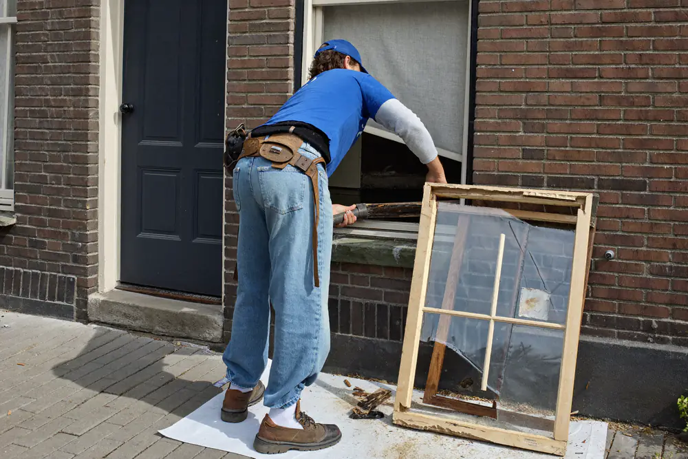 Monteur haalt voorzichtig een oud verrot houten kozijn uit een bakstenen muur